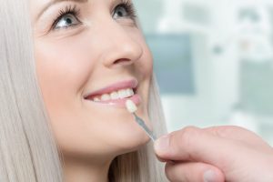 Woman smiling as a dentist holds a veneer in front of her tooth