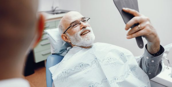 An older man admires his smile in the mirror following periodontal treatments.
