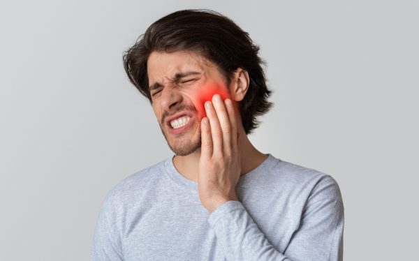 Man experiencing severe dental pain, holding his jaw, indicating a dental emergency related to infection or decay.