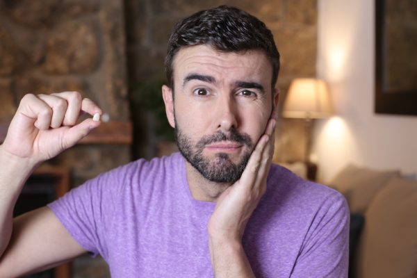 Man holding a pain reliever and touching his cheek, expressing discomfort from a dental emergency.