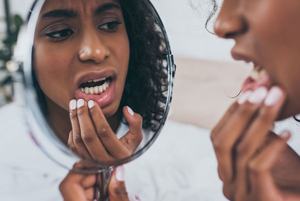 woman looking at her teeth in pain in the mirror